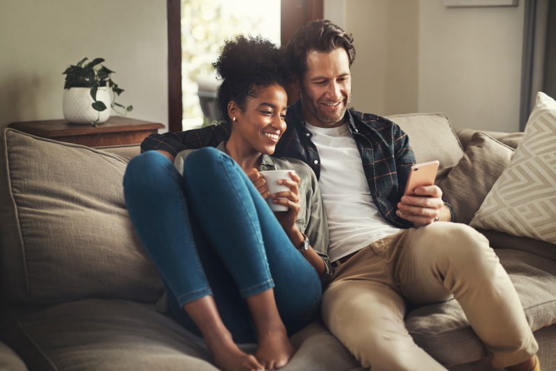 A happy young couple using a digital tablet while relaxing on a couch in their living room at home