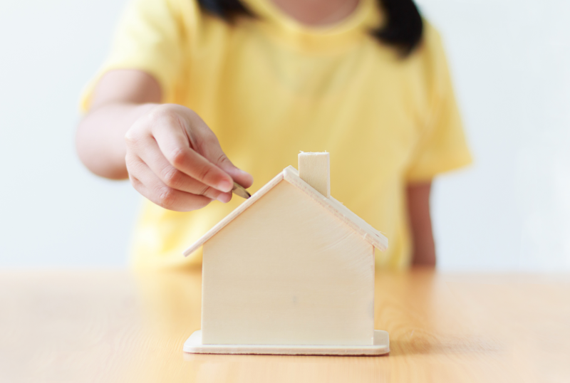 Girl putting a coin in a house shaped piggy bank