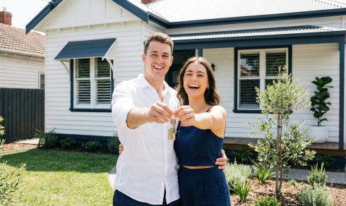 New homeowners holding keys in front of a modern house