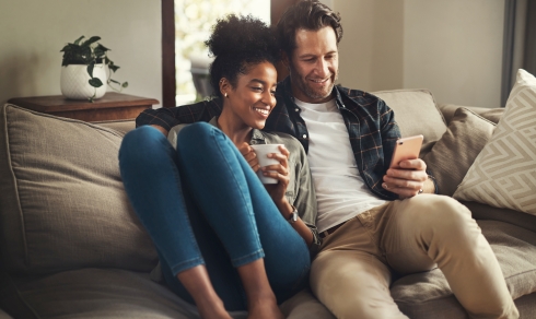 A happy young couple using a digital tablet while relaxing on a couch in their living room at home